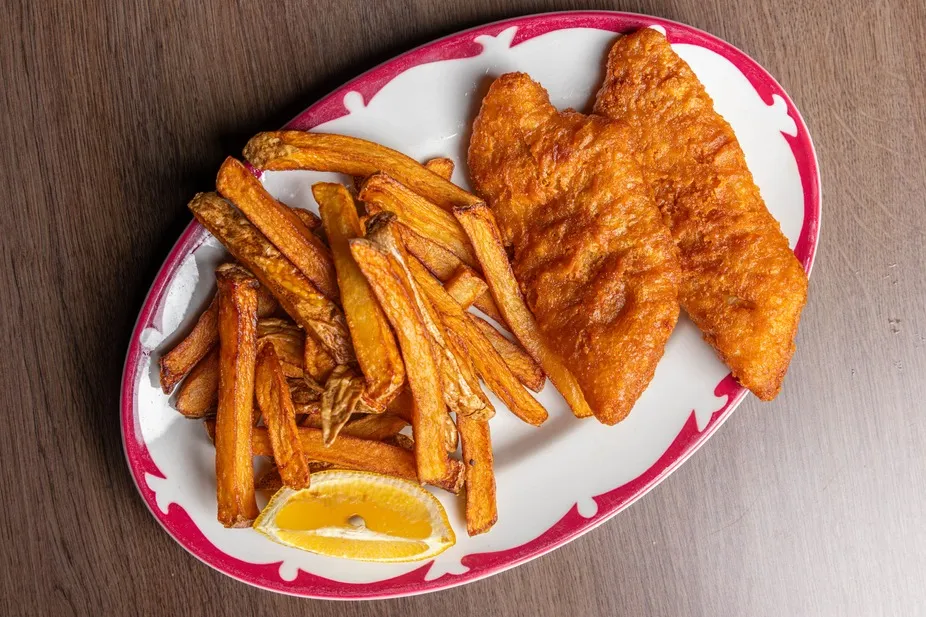 Two pieces of battered fish with fries and lemon