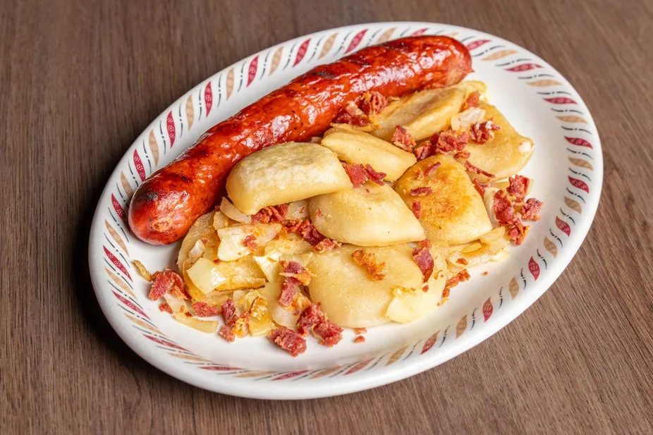 Perogies with bacon bits beside a grilled smokie